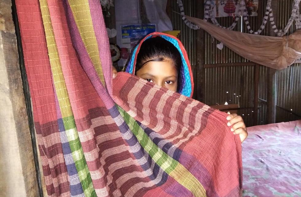  Indien: Ein Mädchen versteckt sich hinter einem Vorhang, nur ihren Kopf ist bis zu den Augen zu sehen.