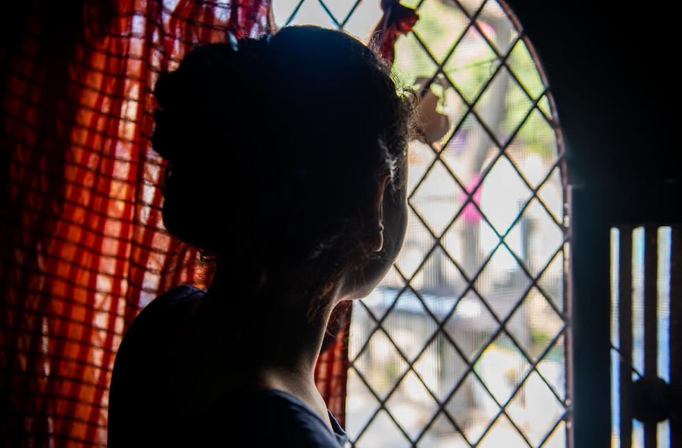 Indien: Ein Mädchen mit hochgebundenen Haaren schaut aus dem Fenster. Ihr Gesicht ist nicht zu erkennen.