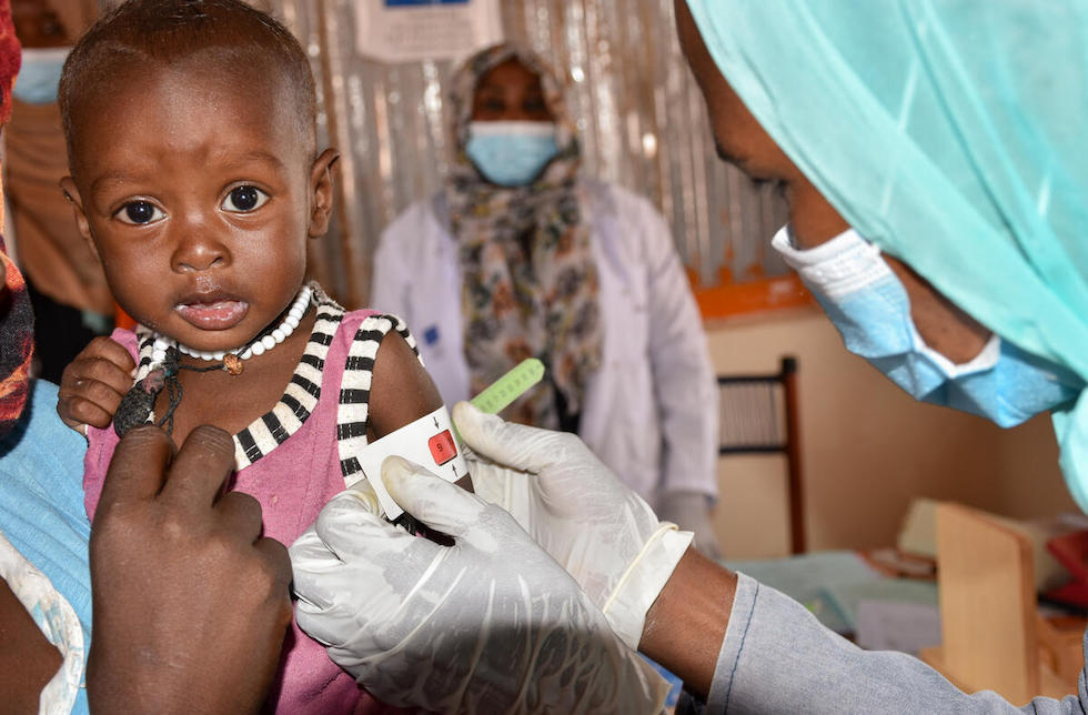 Sudan: Eine medizinische Helferin legt ein Maßband um den Arm eines kleinen Mädchens. Die Skala liegt im roten Bereich.  