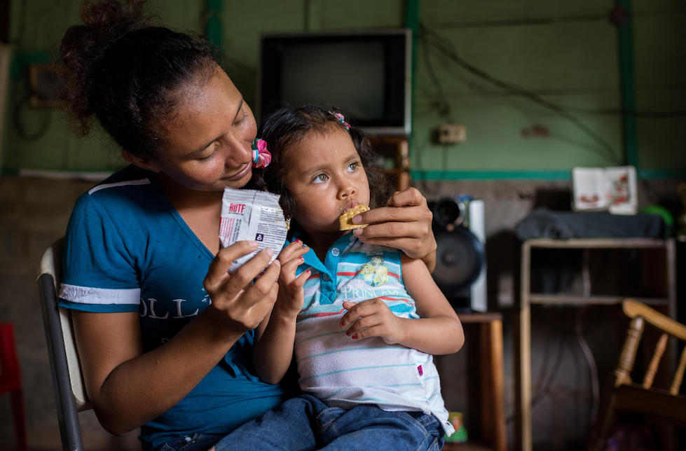 Nicaragua: Ein Mädchen auf dem Schoss ihrer Mutter, wd von dieser mit einem Keks aus einer Plastikpackung gefüttert.