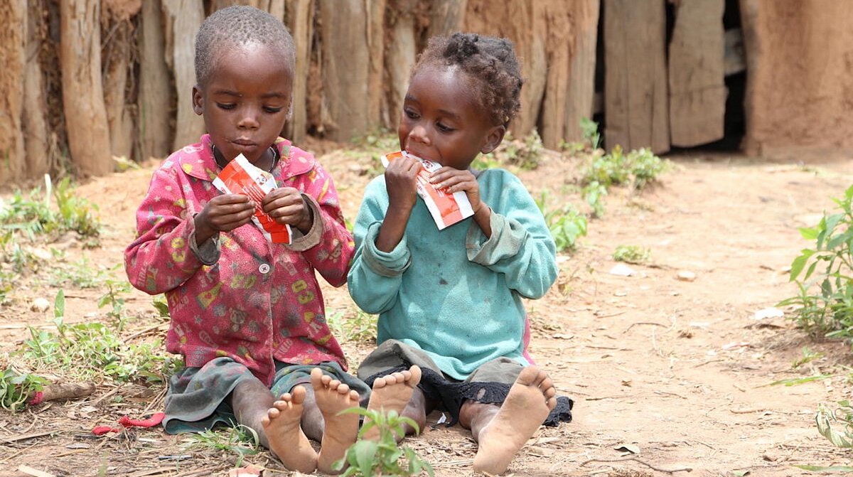 Angola: Die Kinder Pedro (links) und Teresa (rechts) sitzen auf dem Boden und essen Plumpy’nut.