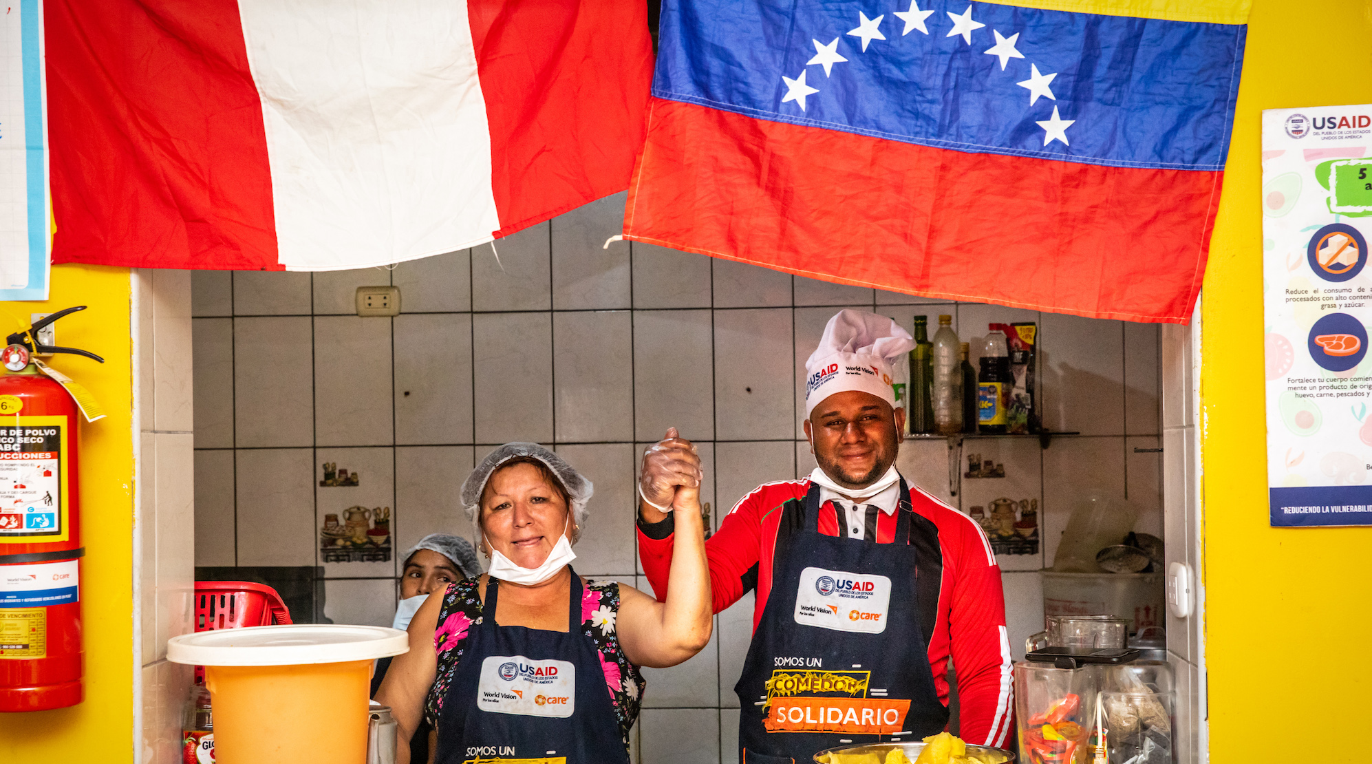 Eine Frau mit Haarnetz und Maske und ein Mann mit Kochmütze stehen gemeinsam an einem Küchentresen.