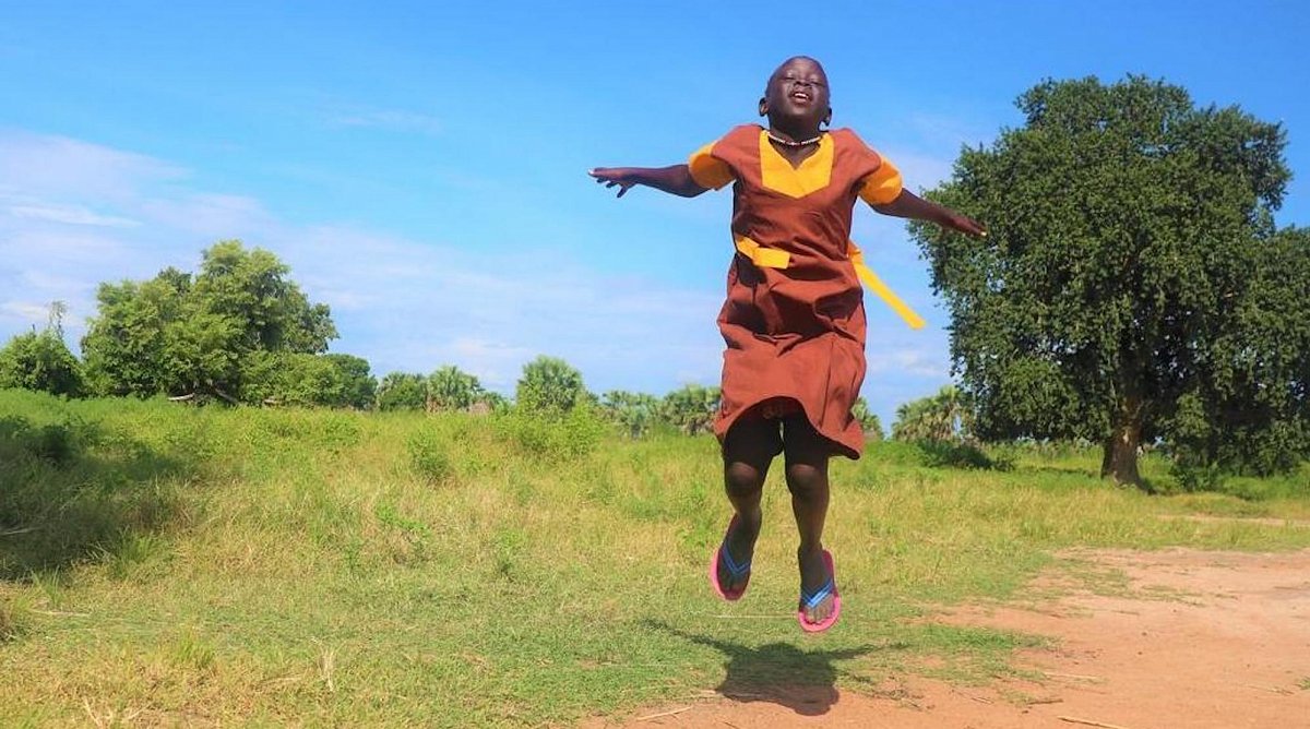 Südsudan: Ajok, 13 in Schuluniform springt mit geschlossenen Augen in die Luft.