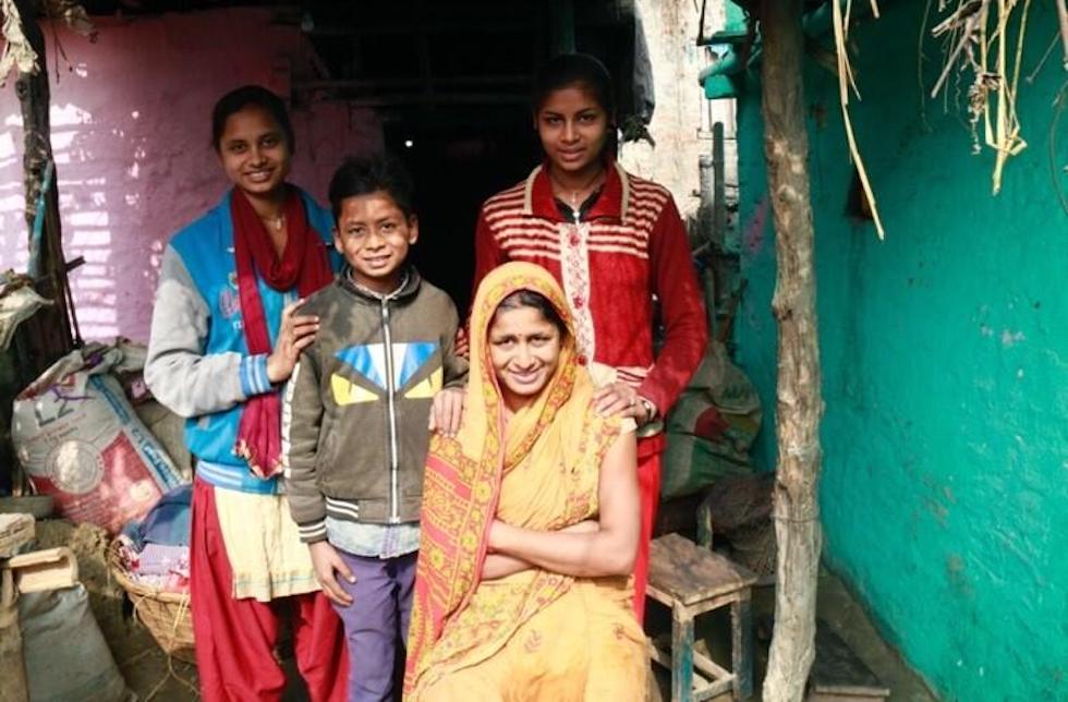 Nepal: Im Vordergrund sitzt Sunita in einem gelben Sari, ihre drei Kinder stehen hinter ihr und legen ihre Hände auf die Schultern ihrer Mutter.