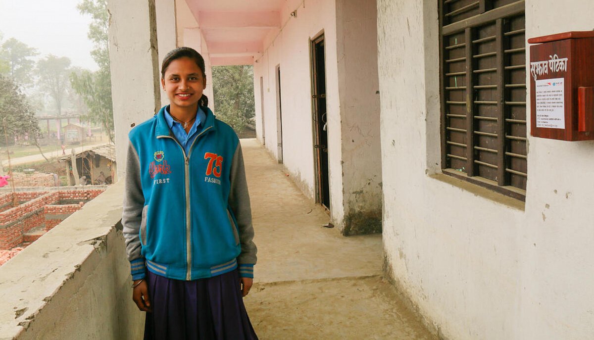 Nepal: Die 16-jährige Pinky vor ihrer Schule in einem Gang und lächelt in die Kamera.