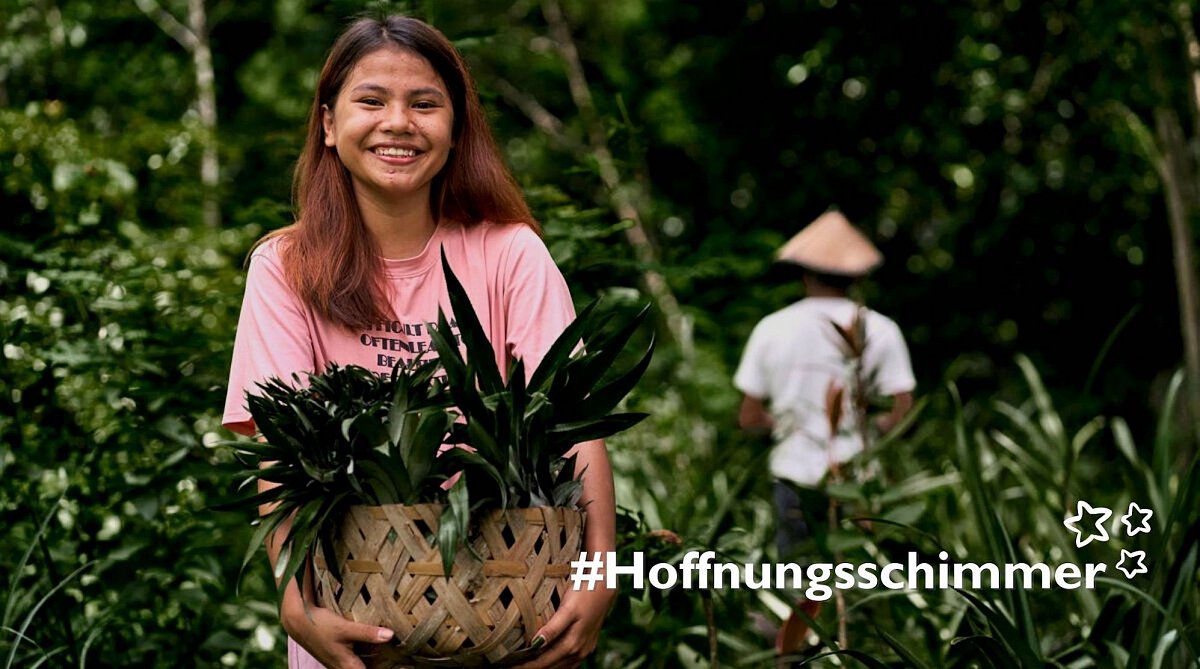Philippinen: Junges Mädchen im pinken Shirt hält einen Korb mit Ananas.