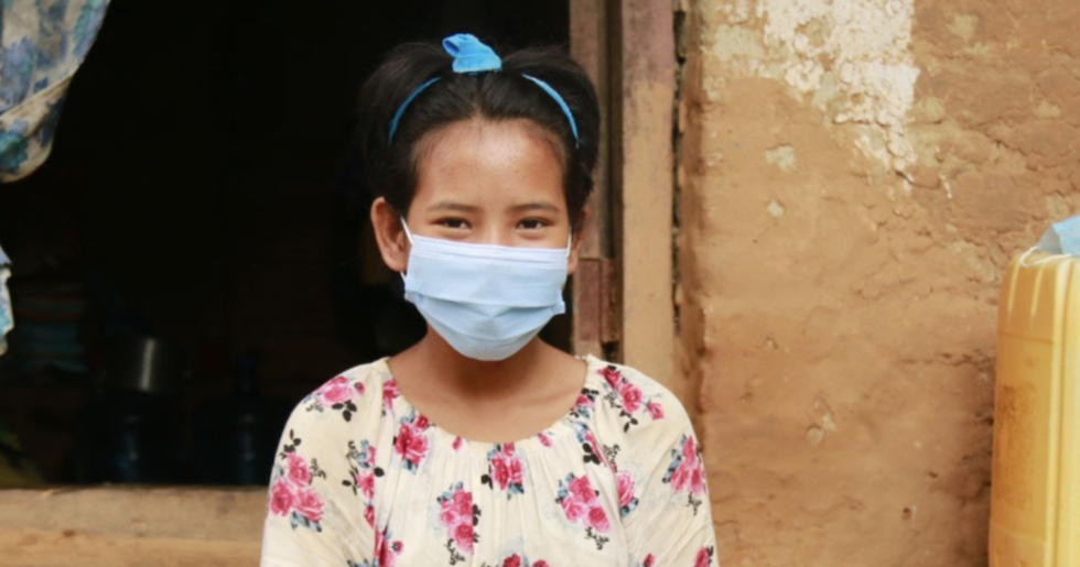 Nepal: Ein junges Mädchen blickt in die Kamera, sie trägt einen Mund-Nasenschutz.