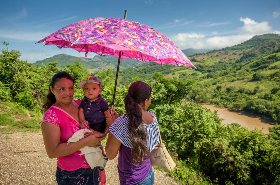 Honduras: Frauen halten ein Kleinkind unter einem Regenschirm, um es vor der Sonne zu schützen.