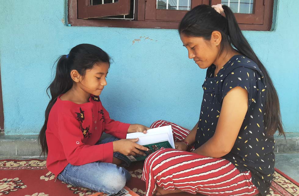 Nepal: Mädchen liest ihrer Mutter aus einem Buch vor.