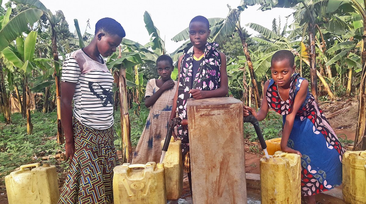 Tansania: Vier junge Frauen holen mit gelben Kanistern Wasser an einem Brunnen.