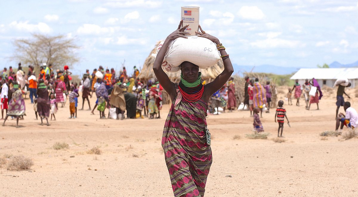 Kenia: Eine Frau trägt Nahrungsmittel auf dem Kopf.