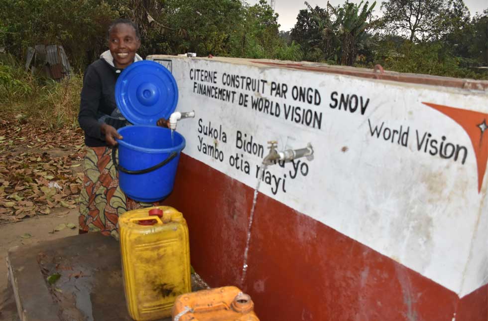 Brigitte steht bei der neuen Zapfstelle für Trinkwasser.
