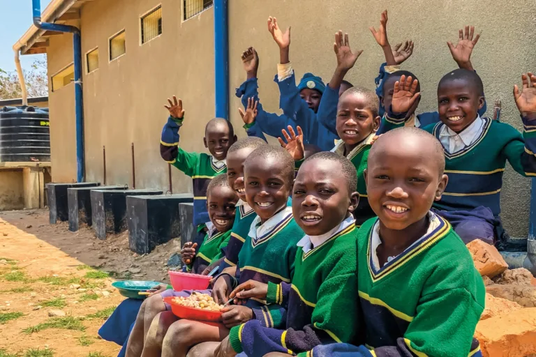 Schulkinder lachen zusammen vor ihrer Schule in Tansania.
