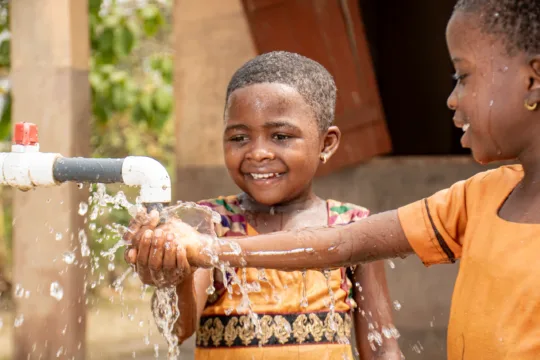 Zwei Mädchen spielen mit dem neuen Wasserhahn in ihrem Schulhaus in Ghana.