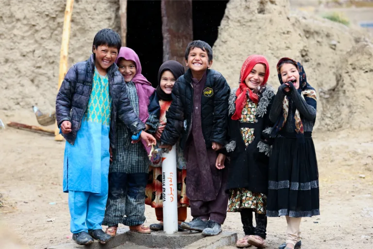 Kinder stehen fröhliche bei einem neuen Trinkwasserbrunnen in Afghanistan