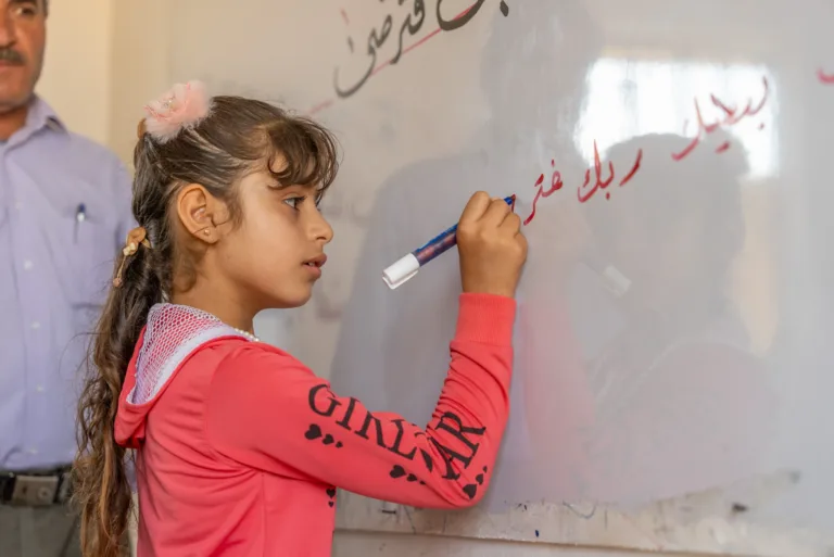Amal schreibt im ländlichen Syrien an ene Wandtafel im wiederhergestellten Schulhaus.
