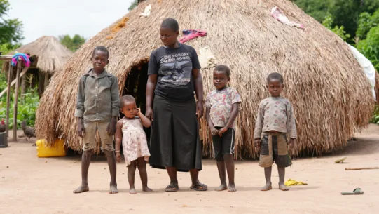 Penina steht mit ihren Kindern vor ihrer Hütte im Südsudan.