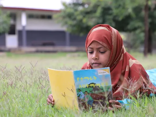 Ein Mädchen liegt in Äthiopien im Gras und liest ein Geschichtenbuch von World Vision.